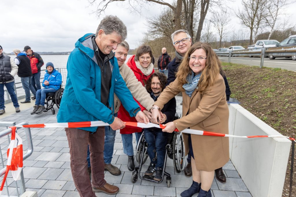 Angler im Rollstuhl und Mitarbeiter des Ruhrverbands eröffnen den barrierefreien Angelplatz am Möhnesee.
